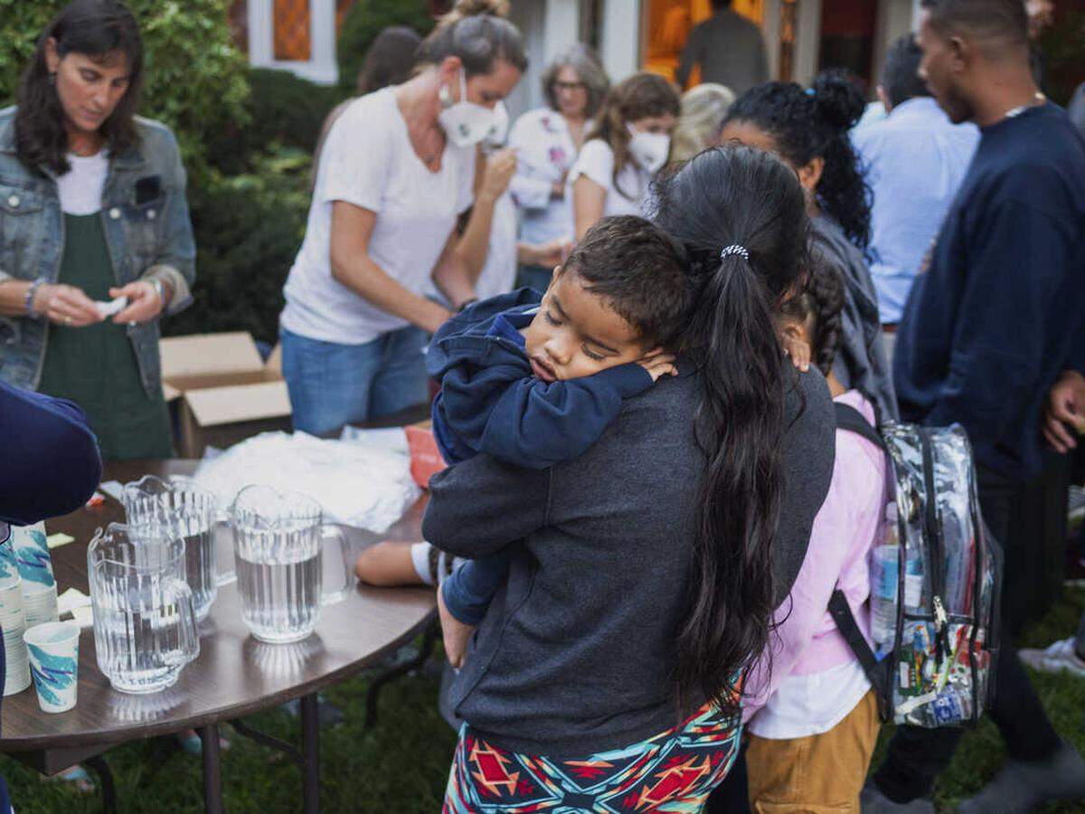 Una mujer,forma parte de un grupo de migrantes trasladados en avión a Martha's Vineyard por el gobernador Ron DeSantis, sostiene a un niño mientras les dan de comer en el exterior de la St. Andrews Episcopal Church, en Edgartown, Massachusetts. Ray Ewing AP