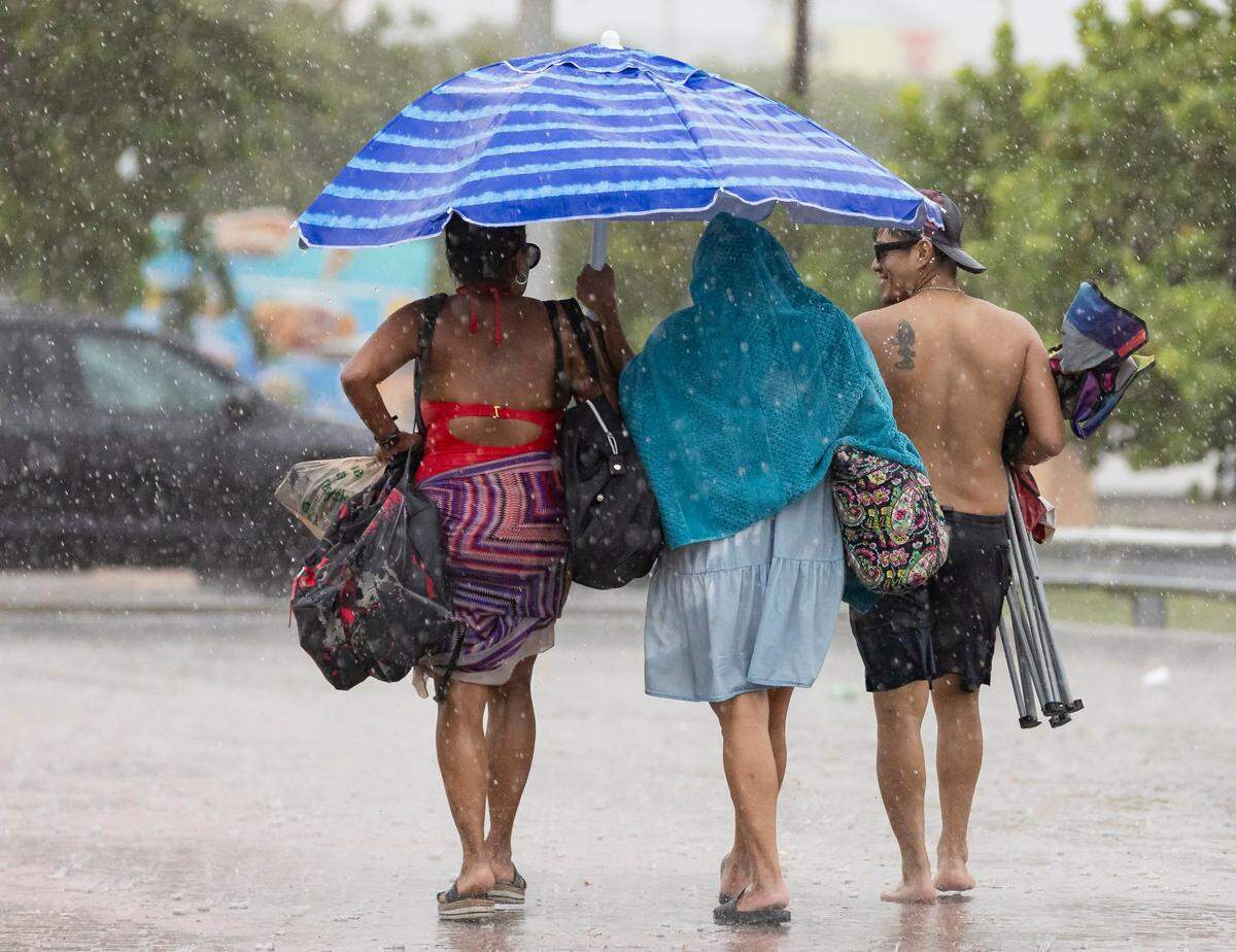 From left to right: Etna Solis, Melida Ortega and Marvin Diaz walk toward their car as lightning and heavy rain falls over Hobie Island Beach Park on Monday, June 19, 2023, in Miami, Fla.