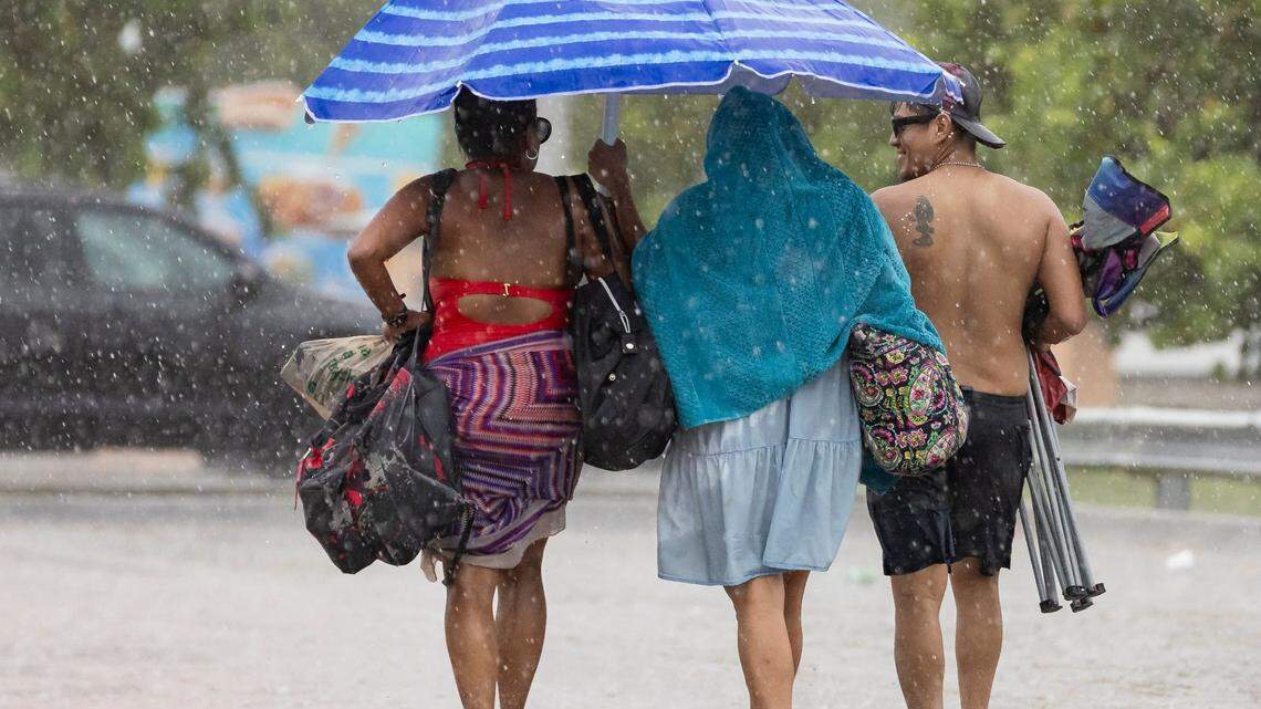 From left to right: Etna Solis, Melida Ortega and Marvin Diaz walk toward their car as lightning and heavy rain falls over Hobie Island Beach Park on Monday, June 19, 2023, in Miami, Fla.