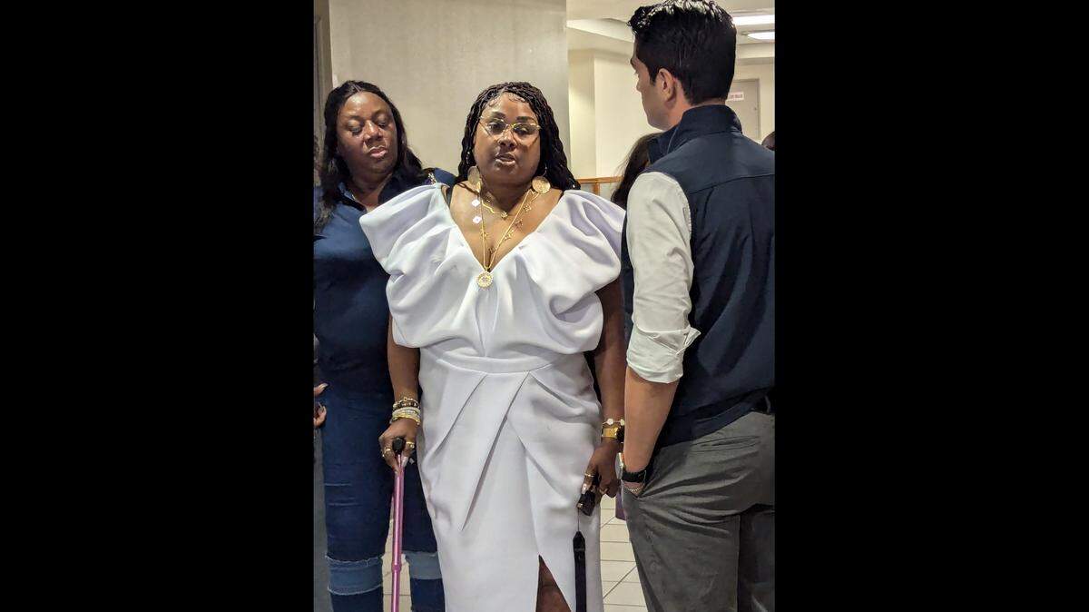 Bridget Knighton, in white dress and with cane, spoke to reporters outside the courtroom where the man accused of shooting her eight times had just been stripped of a plea deal and learned he was to stand trial, Monday, Feb. 3, 2025. The judge’s decision came after emotional testimony from Knighton, who wanted a jury trial.