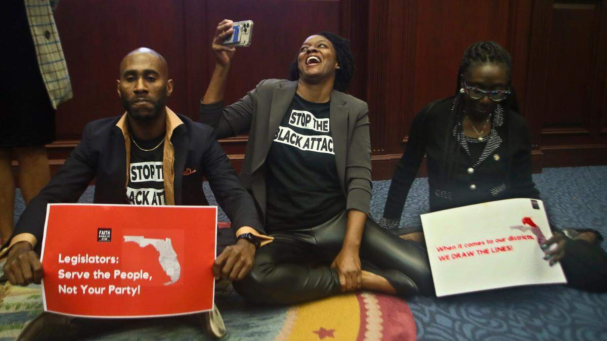 Rep. Tray McCurdy, D-Orlando, Rep. Angie Nixon, D-Jacksonville, and Rep. Felicia Robinson, D-Miami Gardens, sit on the Florida Seal in protest as debate stops on Senate Bill 2-C: Establishing the Congressional Districts of the State in the Florida House of Representatives Thursday, April 21, 2022, at the Capitol in Tallahassee.
