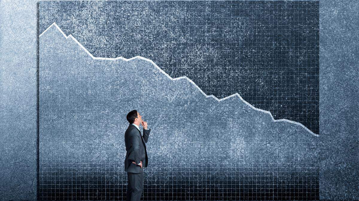 A businessman looking up at a chart on the wall above him that shows declining sales or performance.