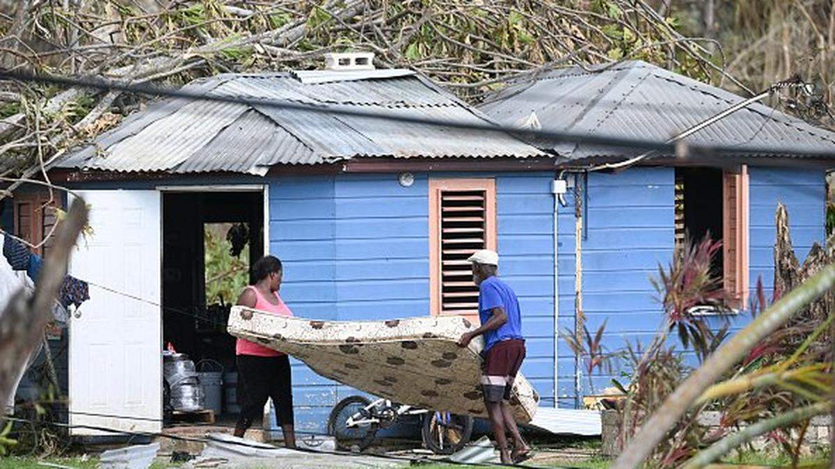 Residents move a mattress from damaged property in the aftermath of Hurricane Melissa in the community of Cave in Westmoreland, Jamaica, on October 31, 2025. At least 19 people in Jamaica have died as a result of Hurricane Melissa which devastated the island nation when it roared ashore this week, a government minister told news outlets late October 31. (Photo by Ricardo Makyn / AFP) (Photo by RICARDO MAKYN/AFP via Getty Images)          