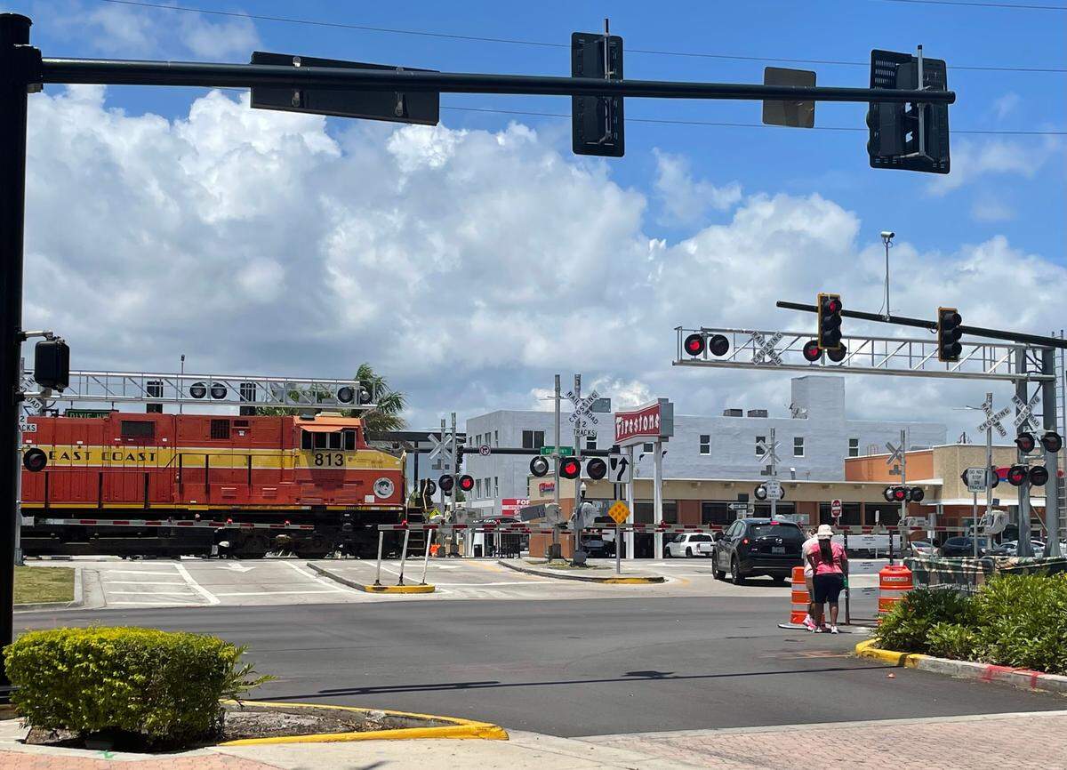 People wait for a passing train before crossing S 21st Avenue and Dixie Highway in Hollywood, Florida on May 9, 2023.