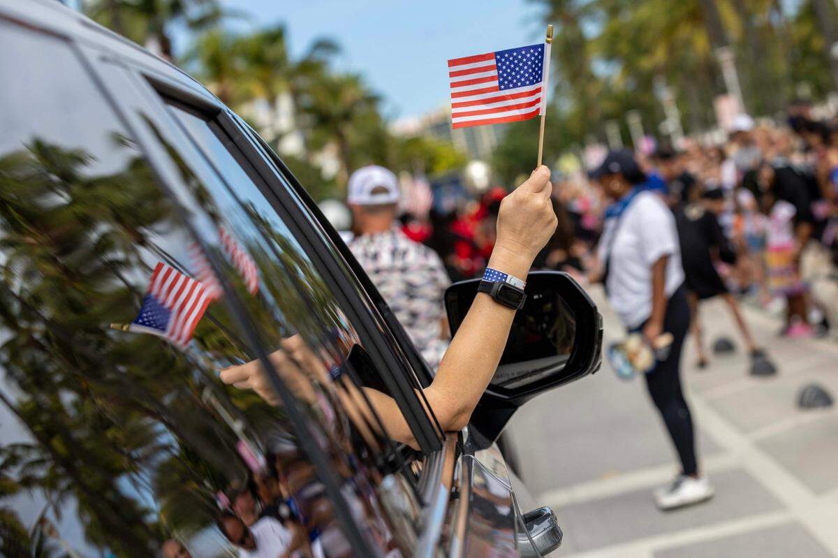 A woman waves an American flag from the window as her car drives up Ocean Drive during the 16th Annual Veterans Day Parade on Monday, Nov. 11, 2024, in Miami Beach, Fla.