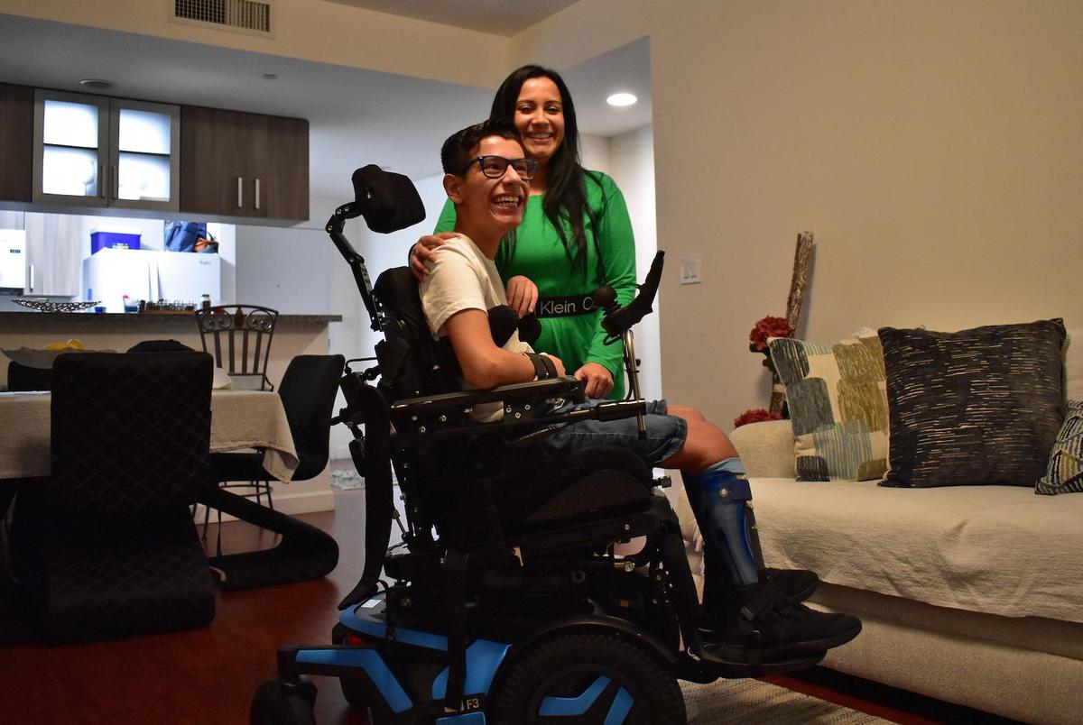 Diana Bustamante and her son, Juan, in their apartment living room. Juan has cerebral palsy, and his mother needs equipment to help lift him from his wheelchair and from his bed.