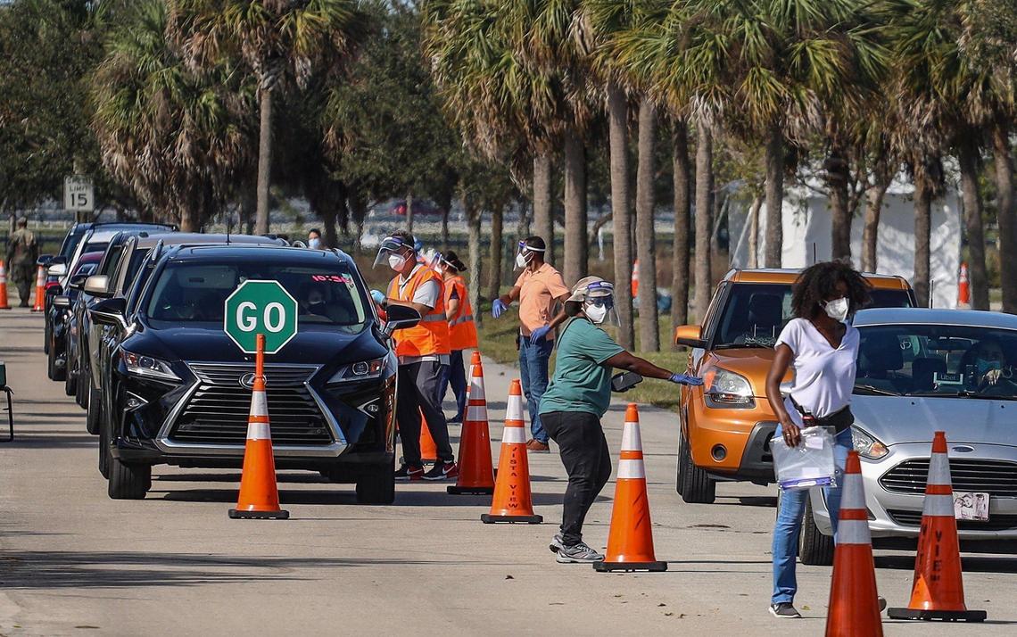 On Sunday, January 3, 2021 motorists line-up for COVID-19 vaccination shots for people who are 65 and older as site staffers assist at Vista View Park in Davie, Florida.