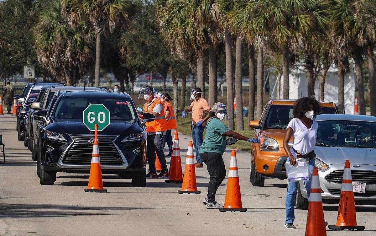 On Sunday, Jan. 3, 2021, motorists line up for COVID-19 vaccination shots for people who are 65 and older as site staffers assist at Vista View Park in Davie, Florida.