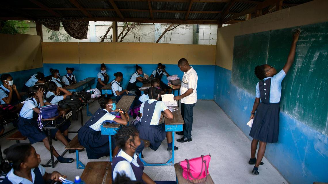 A student erases the chalkboard as the teacher talks to students who have returned to school amid the COVID-19 pandemic at Lycee Marie Jeanne in Port-au-Prince, Haiti, Monday, Aug. 17, 2020.