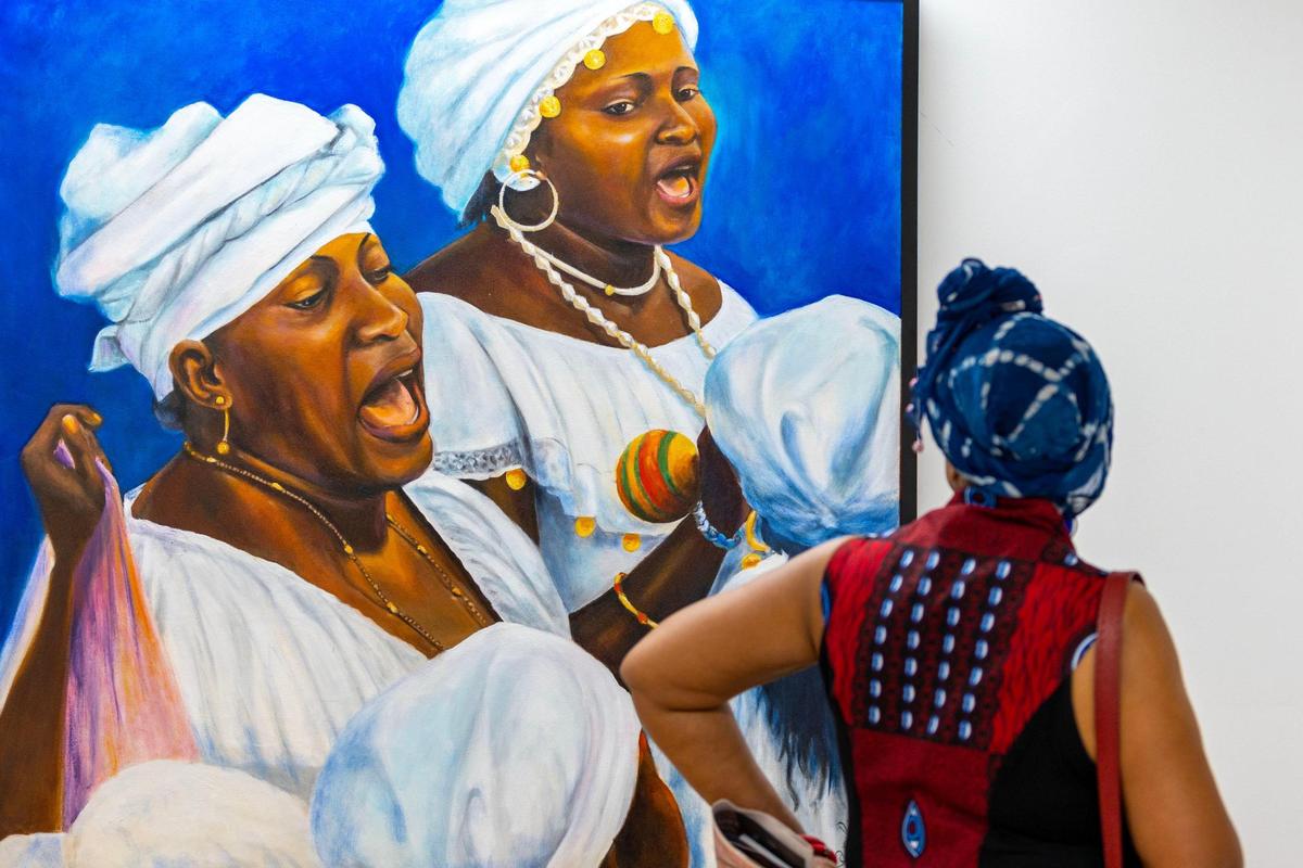 A woman looks at a painting entitled ‘Singing Hounsies’ by artist Carl Craig during the Preview for The Art of Transformation.