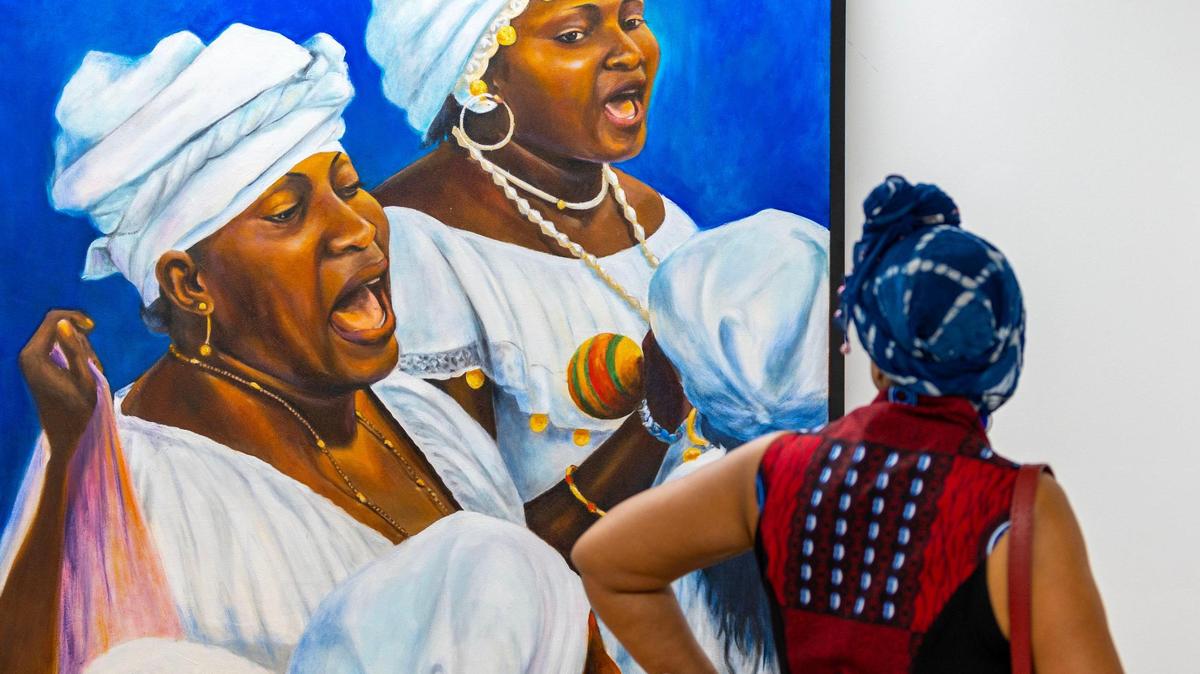 A woman observes a painting entitled ‘Singing Hounsies’ by artist Carl Craig during the Preview for The Art of Transformation.