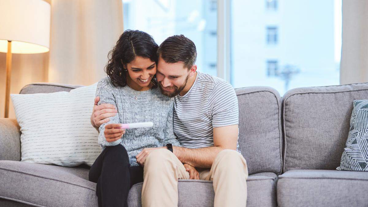 Cropped shot of a happy young couple sitting on the sofa together and holding a positive pregnancy test