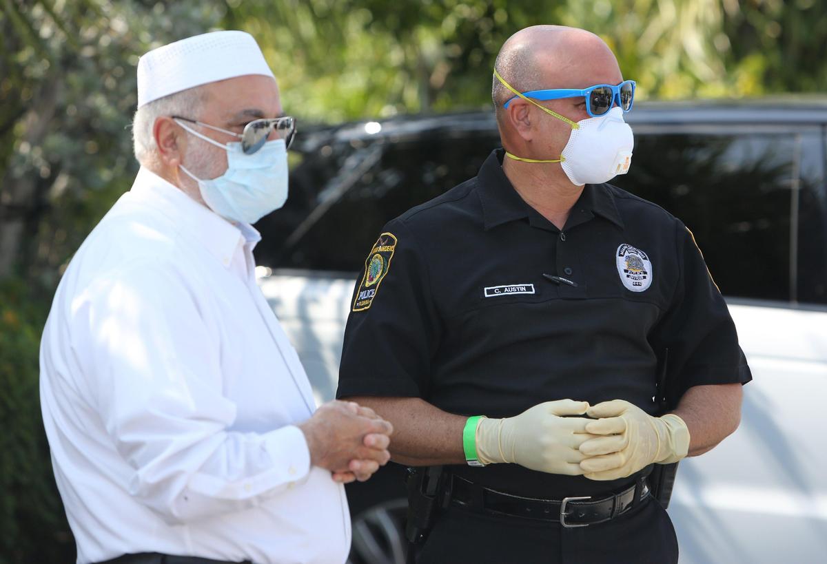 Imam Dr. Abdul Hamid Samra talks with Miami Gardens police officer Carlos Austin as they watch dozens of cars drive through the parking lot of the Islamic Center of Greater Miami to collect food. Since Muslims can’t gather together to celebrate Ramadan, the members of the Islamic Center of Greater Miami created a drive-through food distribution at their Miami Gardens mosque Tuesday, April 21, 2020. The mosque will continue the distribution each week for the next several weeks.