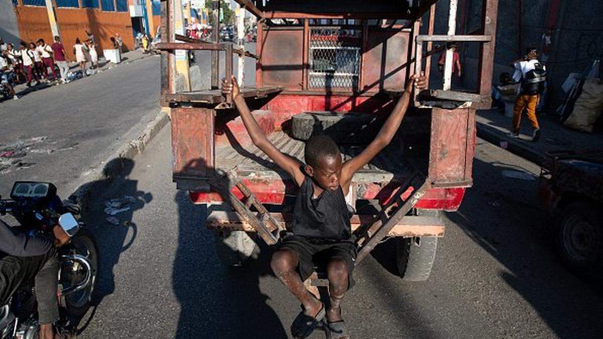 A child hangs on the back of a van as it drives through downtown Port-au-Prince, Haiti, on February 13, 2026. Haiti's presidential transitional council, which has run the impoverished Caribbean nation for nearly two years, on February 7, 2026, handed power to US-backed Prime Minister Alix Didier Fils-Aime, after failing to rein in rampant gang violence.  The transfer of power between the nine-member council, created in April 2024, and 54-year-old businessman Fils-Aime took place under tight security, given Haiti's unstable political climate. (Photo by Clarens SIFFROY / AFP via Getty Images)