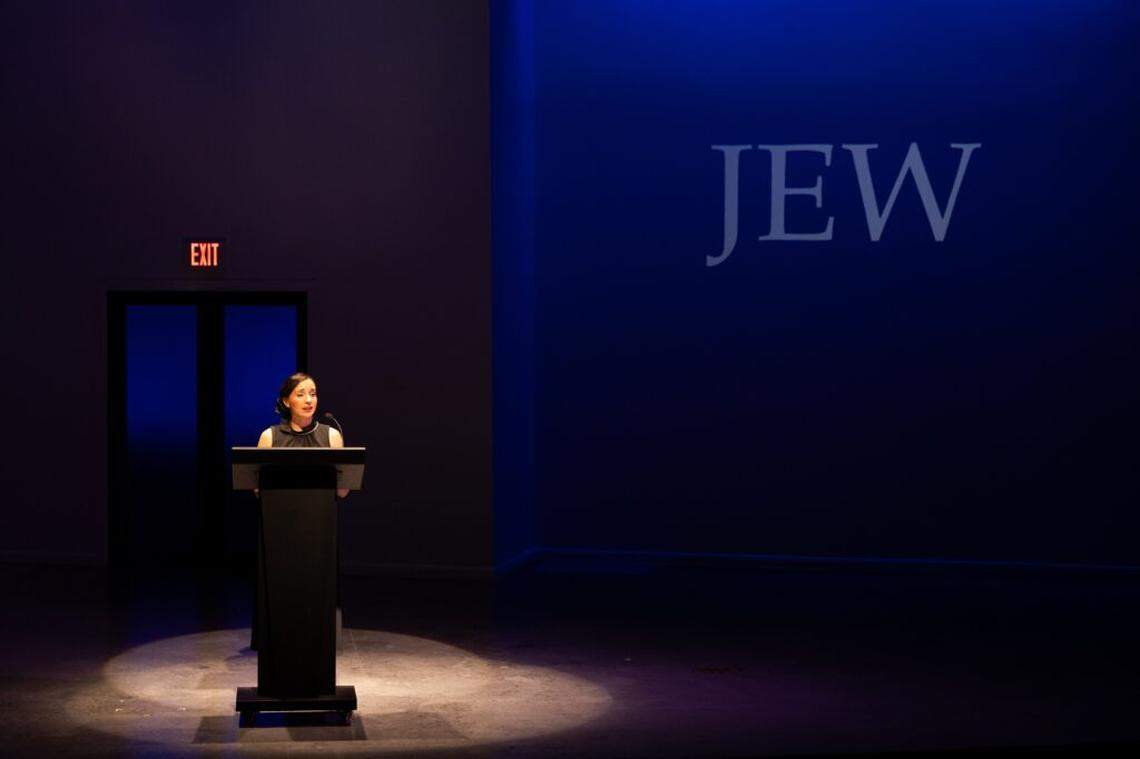 Krystal Mille Valdes as the assistant delivers a message from David, the artist, about why he’s transformed into a dog.