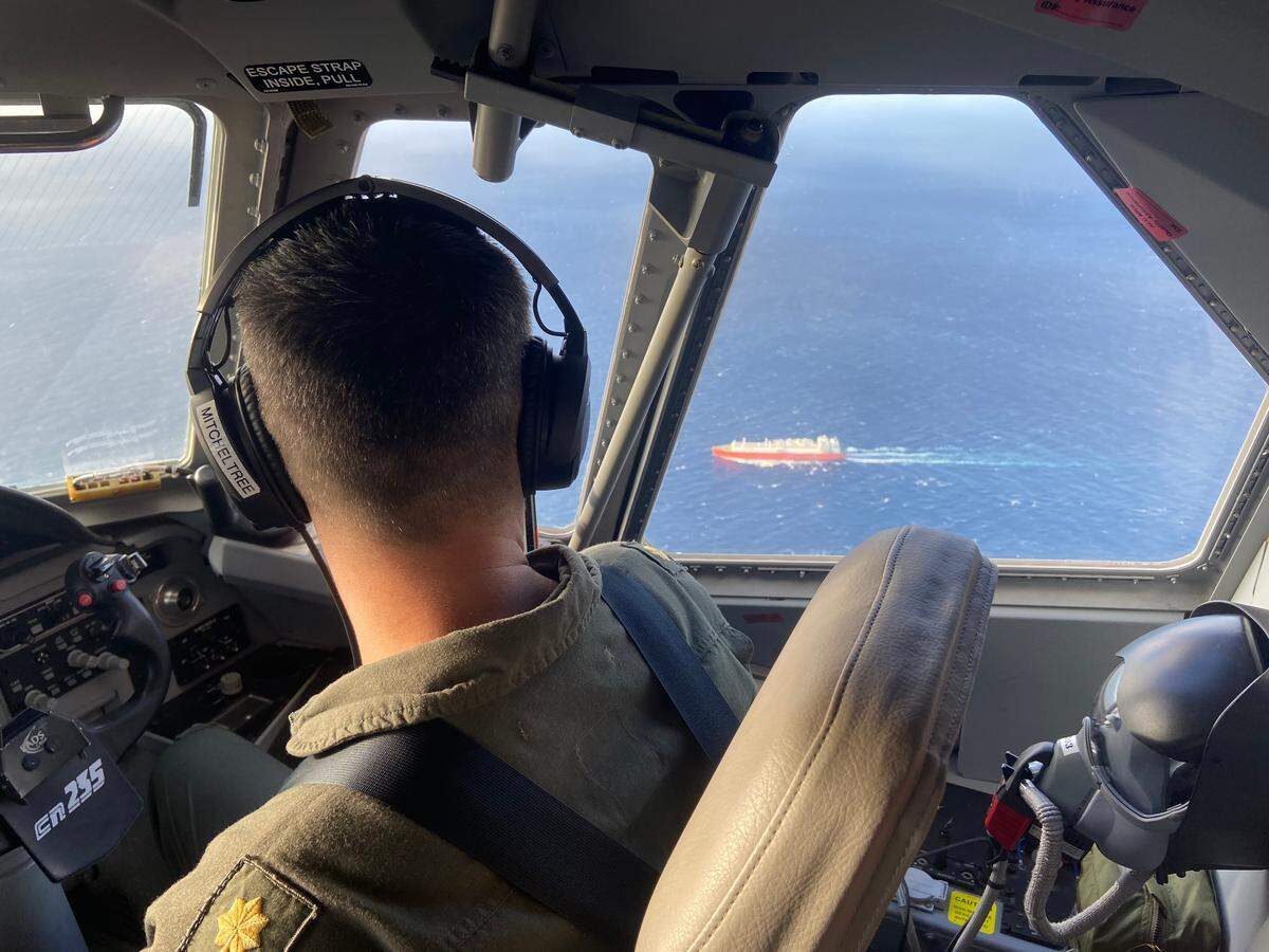El piloto de la Guardia Costera de Estados Unidos, teniente comandante Joshua Mitcheltree, vuela un C-144 Ocean Sentry sobre el Estrecho de la Florida, el sábado 14 de enero de 2023, mientras un buque de carga navega en el agua por debajo.