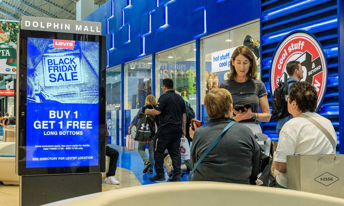 Shoppers walk by sales discount banners at Dolphin Mall in Miami, ahead of the Black Friday sale event, on Friday, Nov. 21, 2025.