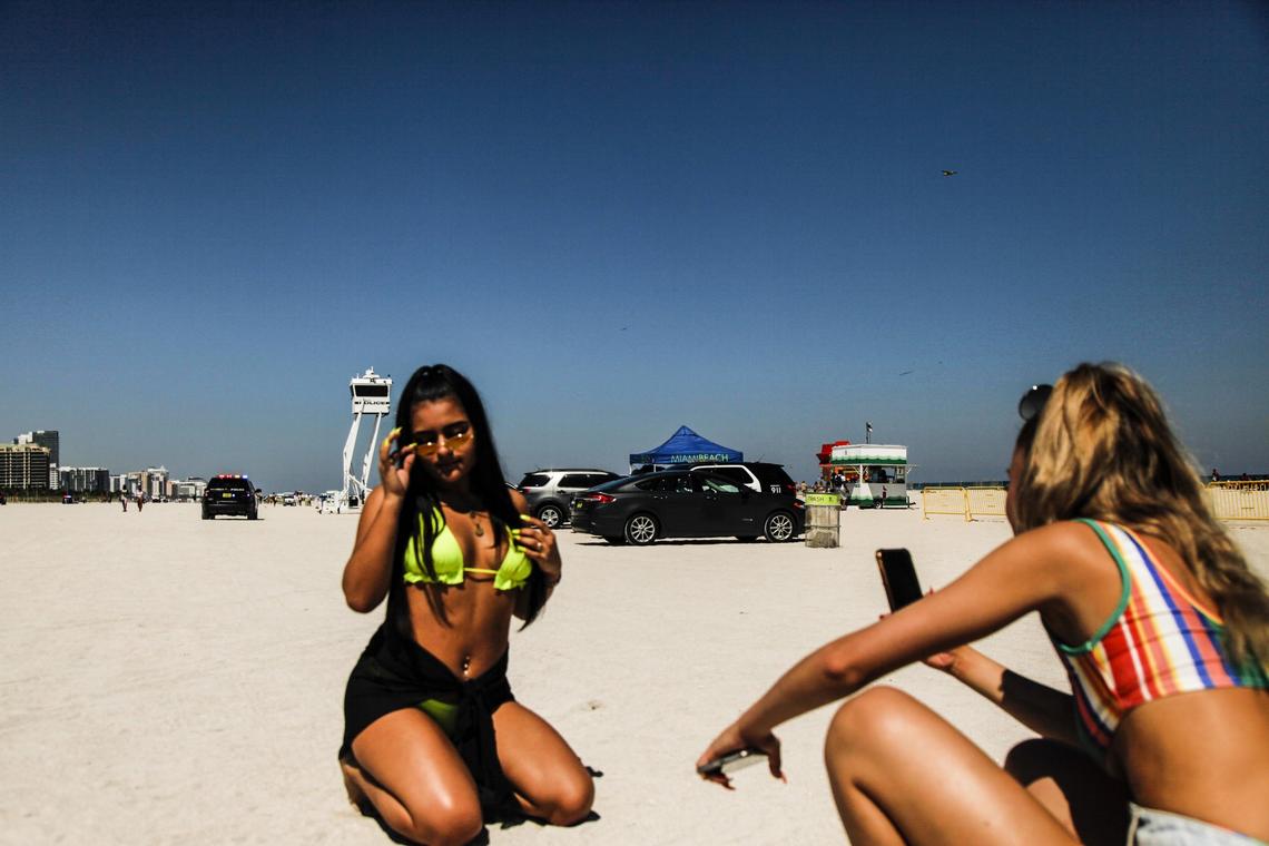 Daniella Guevara, left, poses as Emma Channavier takes a photo on South Beach Friday. Behind them are a dozen Miami Beach police vehicles monitoring the beach.