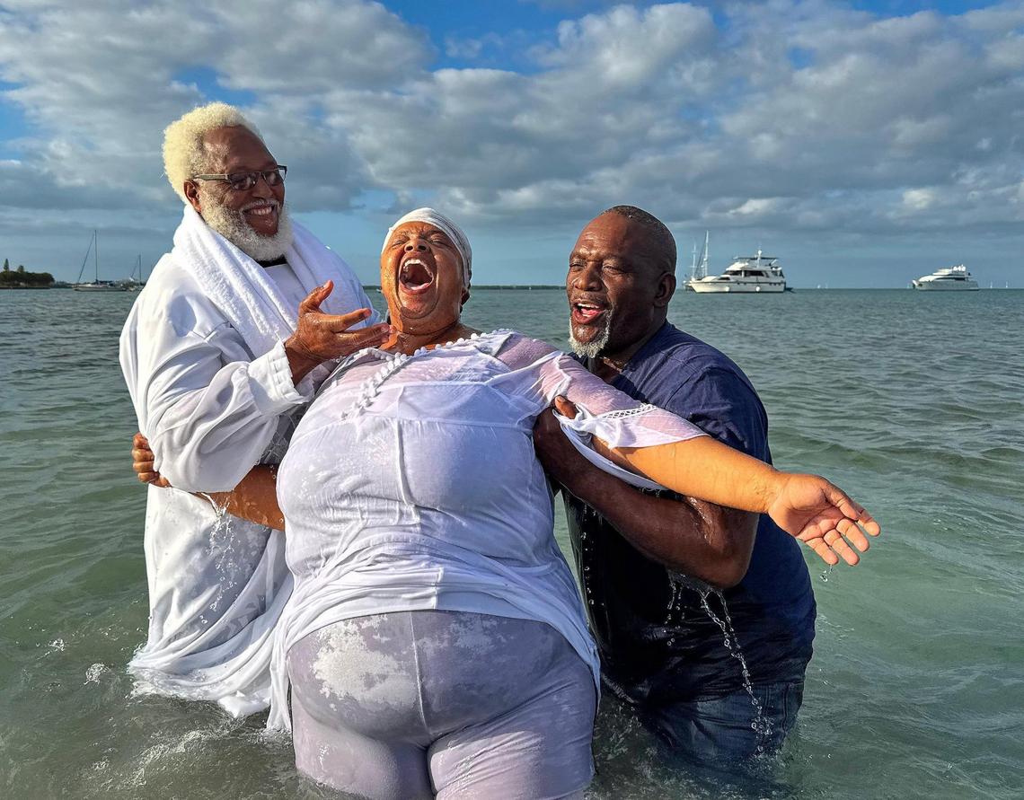 Bettye Hardy, center, member of the Jesus Christ True Church shouts in joy after being baptized by Minister Allen Mushgrove, left, and Apostle Leon Everett, right, on Hobie Beach.