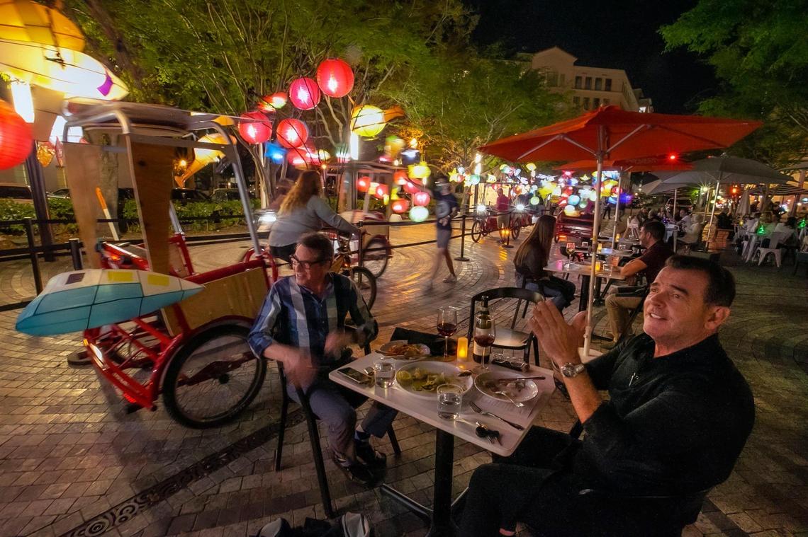 Burton Hersh and Ralph Cabrera, left to right, watch glowing pedicabs, called ‘Fireflies,’ illuminate Giralda Plaza as they enjoy outdoor dining in the heart of Downtown Coral Gables on Tuesday, March 2, 2021.