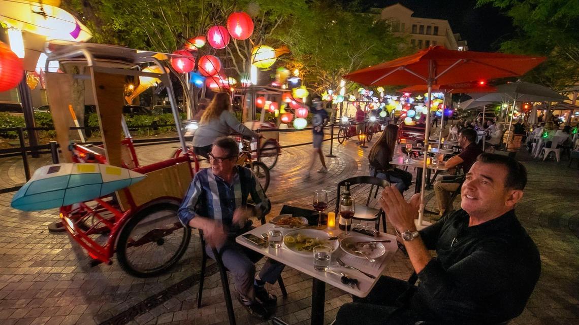 From left, Burton Hersh and Ralph Cabrera watch glowing pedicabs, called ‘Fireflies,’ illuminate Giralda Plaza as they enjoy outdoor dining in the heart of Downtown Coral Gables on Tuesday, March 2, 2021.