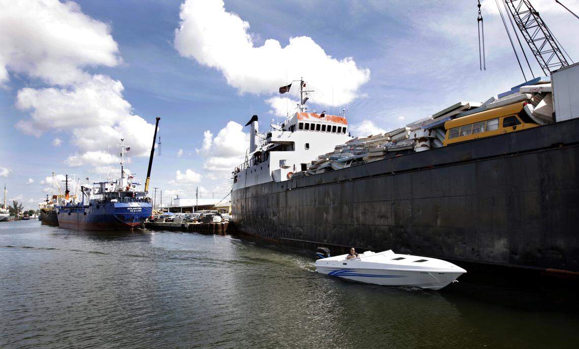 A boater in a speedboat heads down the river past cargo ships loaded with supplies.