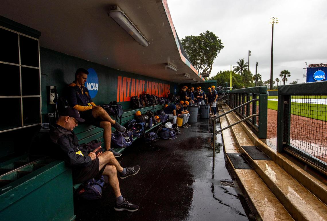 Canisius College players and staff sit in the visitors dugout while it rains after the University of Miami baseball team was forced to postpone the first round of the NCAA Division I Baseball Tournament due to weather at Alex Rodriguez Park at Mark Light Field in Coral Gables, Florida, on Friday, June 3, 2022. The Coral Gables Regional has been moved to Saturday, June 4th.