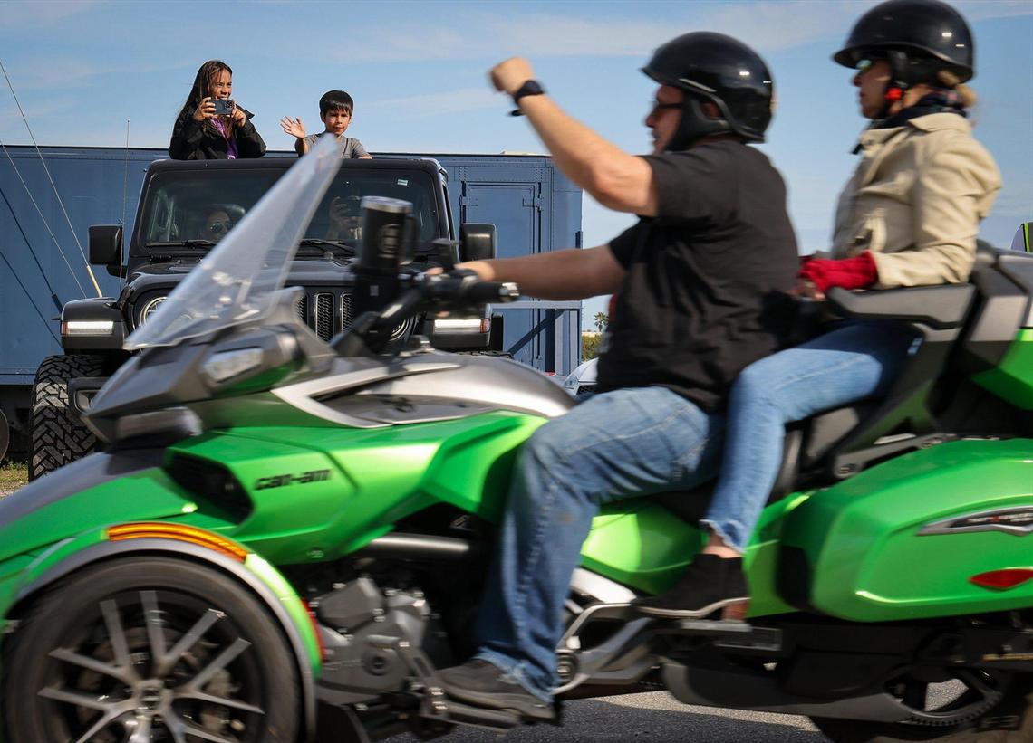 Diana, left, captures riders as Santiago, center, waves as they stand through the car’s moon roof as approximately 350 riders took part in the 13th Annual Archbishop Motorcycle Ride, a fundraiser aimed at raising funds for the St. Luke’s Center, an organization focused on eradicating addiction on Sunday, January 26, 2025, in Doral, Florida. Note: Diana would not release their last names.