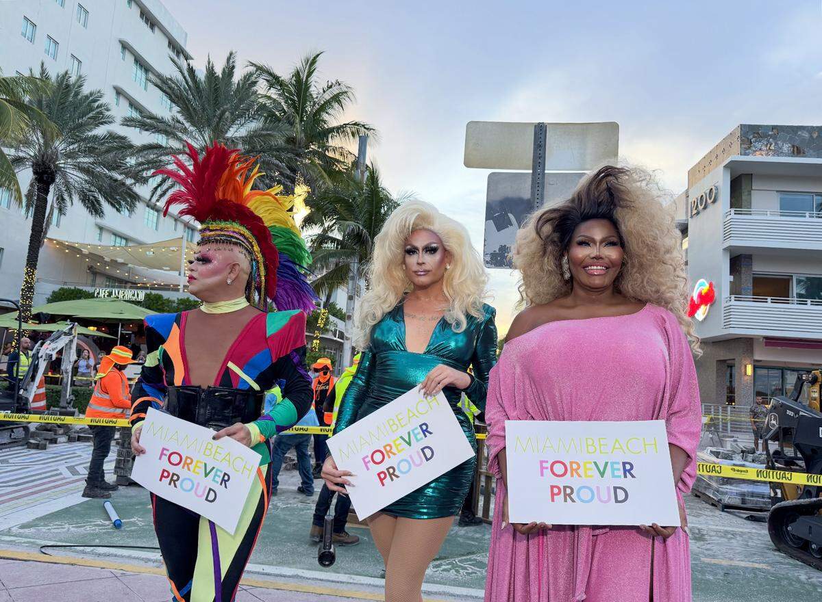 From left to right TP Lords, CC Glitzer and Akasha O’Hara Lords pose for a photo holding “Miami Beach Forever Proud” signs as FDOT removes a rainbow-themed crosswalk.