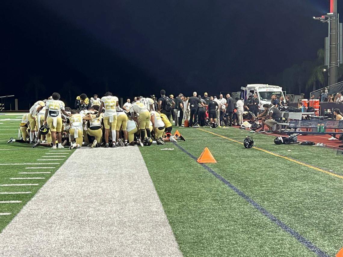 Players from St. Thomas Aquinas and Western’s football teams gather in silent prayer as a Western player is attended to by medical staff on the sideline during the two schools’ game on Thursday at St. Thomas Aquinas.