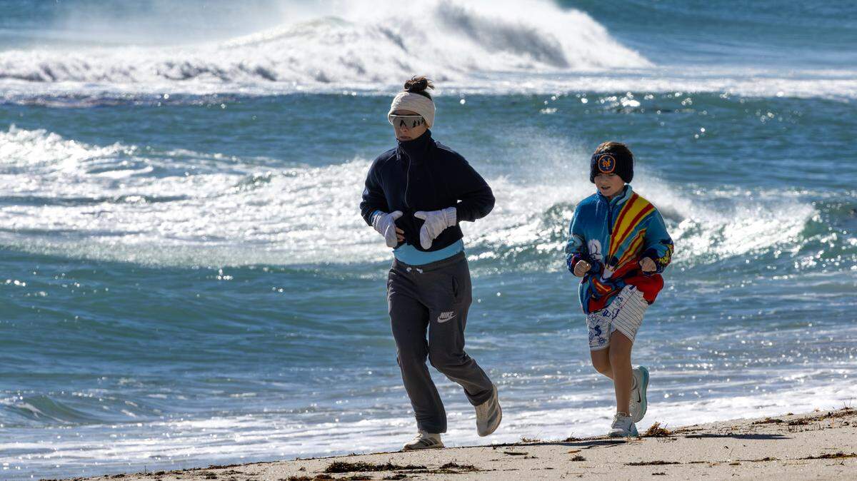 South Florida resident Stephanie DeFrancesco runs with her son, Ari Sella, as they bundle up against the cold on the beach in Sunny Isles Beach, Florida, on Sunday, Feb. 1, 2026. Miami-area temperatures dipped into the 30s.