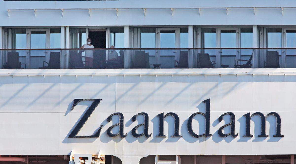 Passengers wearing face masks stand on their balcony as the Zaandam cruise ship with COVID-19 passengers on board is escorted into Port Everglades on April 2, 2020, after 12 days at sea searching for a place to dock. It was escorted into port along with its sister ship, the Rotterdam.