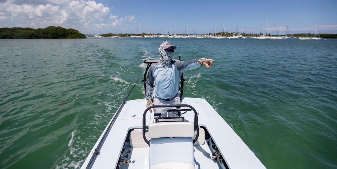 Fishing guide Carl Ball, 58, points while driving his boat near Crandon Park Marina on Saturday, April 22, 2023, in Key Biscayne, Fla.