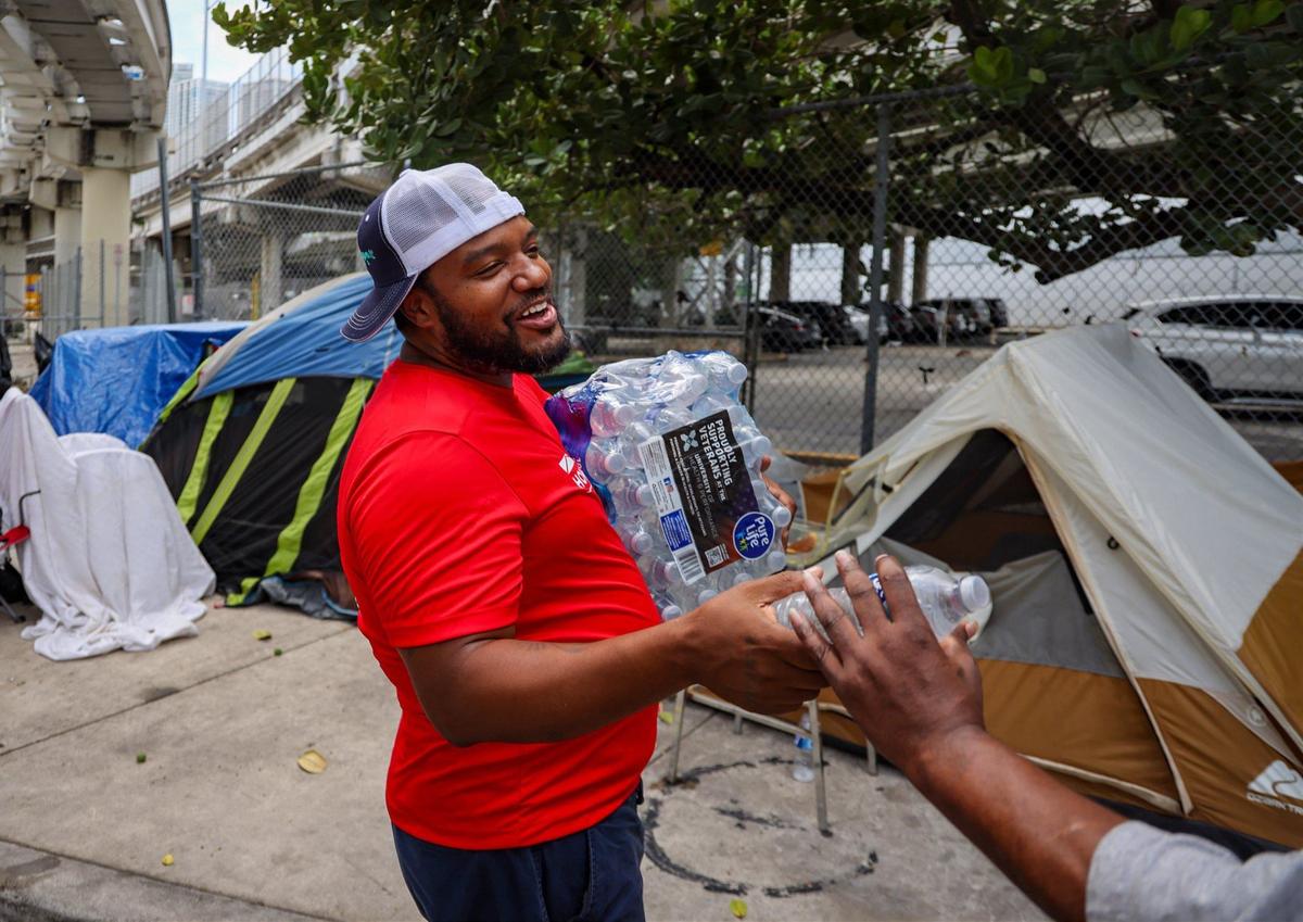 Outreach worker Denny Baldonado, 40, hands out water as members of his team survey the downtown and offered services to unhoused individuals on the street on Thursday, August 1, 2024, in Miami, Florida.