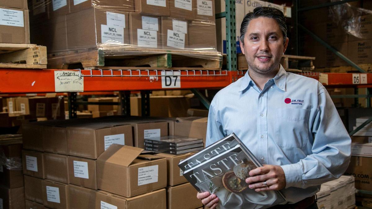Ryan Schoeneck, Chief Operating Officer of J.M. Field Marketing, holds a couple of Crystal Cruises cookbooks that were produced during the pandemic. J.M. Field Marketing produces, packs and ships marketing material for the cruise industry.