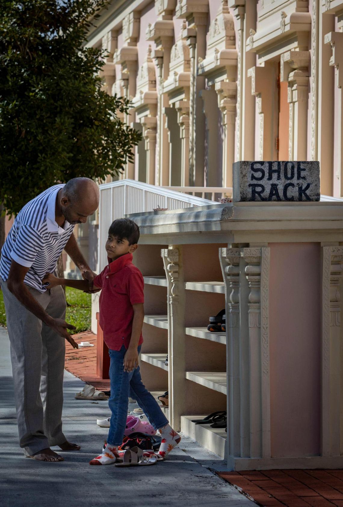 A man helps a boy remove his shoes before entering the Shiva Vishnu Temple of South Florida, a traditional South Indian Hindu Temple.