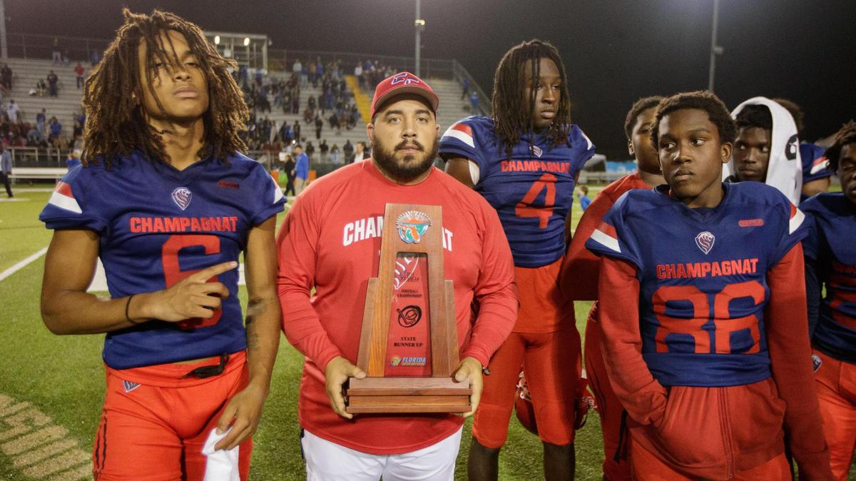 Champagnat head coach Hector Clavijo and players stand together for a photo with their runner-up trophy. Trinity Christian defeated Champagnat 41-23 to claim the Class 2A State Championship title at Gene Cox on Thursday, Dec. 9, 2021.