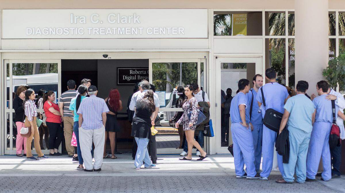 People and hospital personnel stand outside the main entrance of Jackson Memorial Hospital after a possible threat inside the hospital on Monday, July 2, 2018.