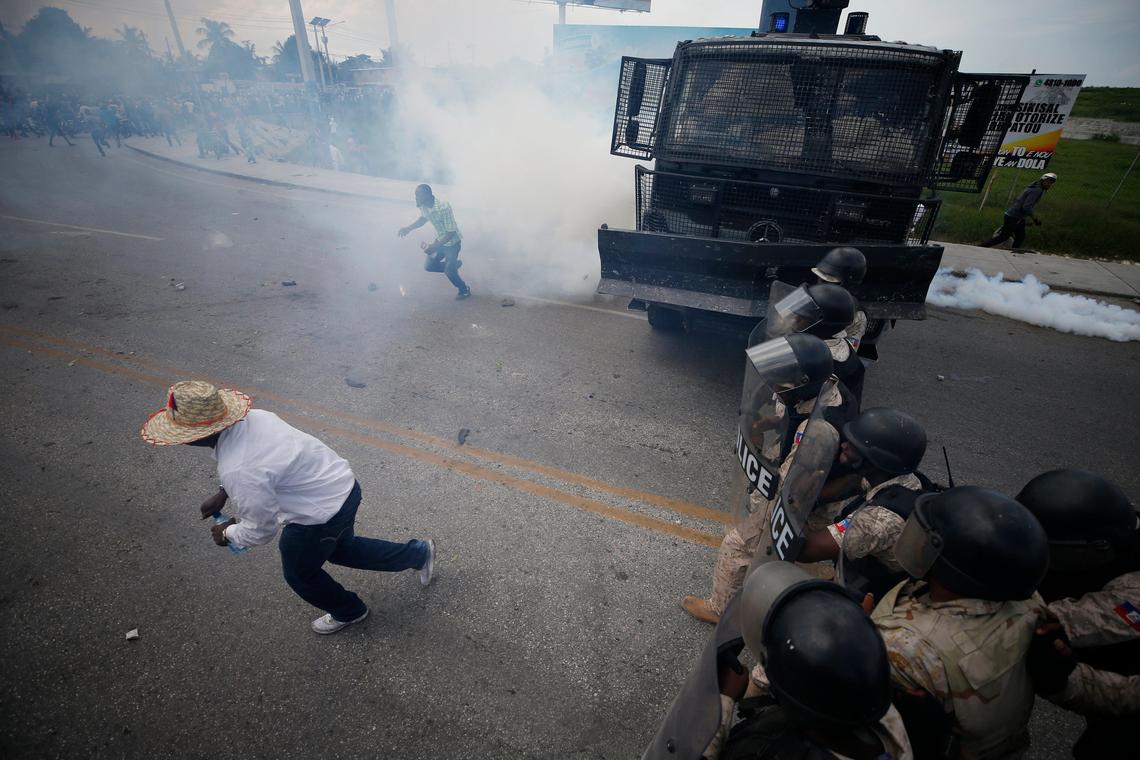 Demonstrators run from a cloud of tear gas after a scuffle with the police during a protest calling for the resignation of President Jovenel Moise, near the airport in Port-au-Prince, Haiti, Friday, Oct. 4, 2019.