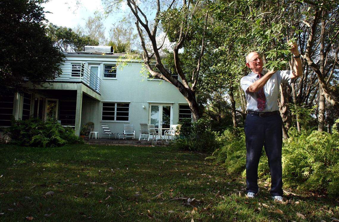 Jack Parker examines a tree in his yard that provides shade and helps funnel breezes into his windows in this 2003 photo. The trees also act as a sound buffer and bring in native wildlife. On top of the roof, a passive solar hot water system provides nearly all of the house’s hot water, and light-colored shingles reflect heat and save energy.