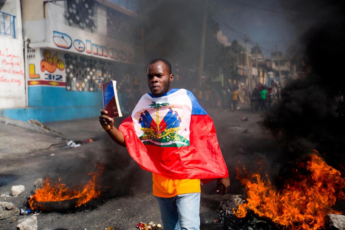 A demonstrator draped in the Haitian flag holds up a copy of the Haitian constitution during a protest to demand the resignation of President Jovenel Moise in Port-au-Prince, Haiti, Thursday, Feb. 7, 2019.