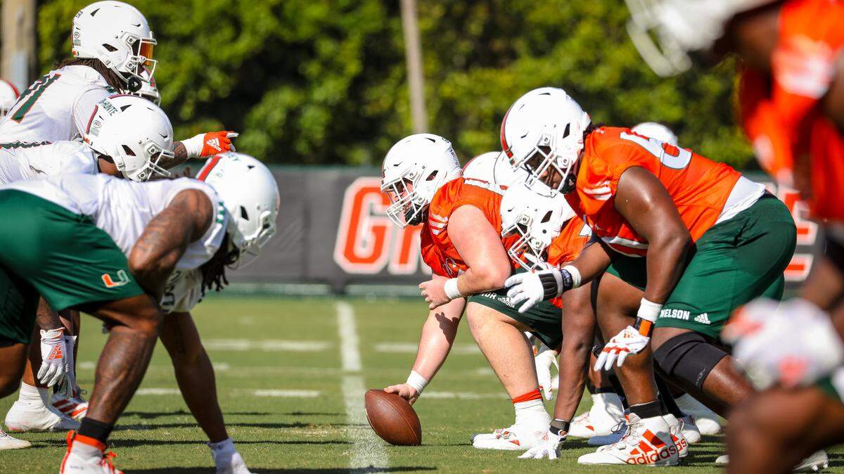 The Miami Hurricanes offensive line, wearing orange jerseys, lines up against the defense during spring practice on March 16, 2021. Zion Nelson, UM’s left tackle, is in the foreground.