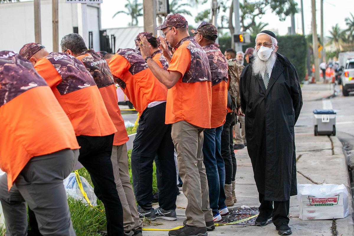 Rabbi Sholom D. Lipskar, founder of the Shul of Bal Harbour, walks by members of the Christian group Legendarios Saturday, as they pray for the victims and the families of the Champlain Towers South Condo that collapsed Thursday, June 24th, in Surfside.