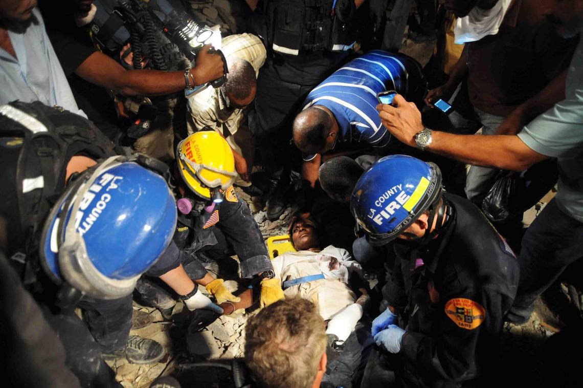 Roger Sainfort (in striped shirt) checks on his wife, Ginette Sainfort, while members of the Los Angeles County Fire Department Search and Rescue Team give her an IV following her rescue from the parking lot of a collapsed three-story bank. She spent nearly a week buried in rubble.