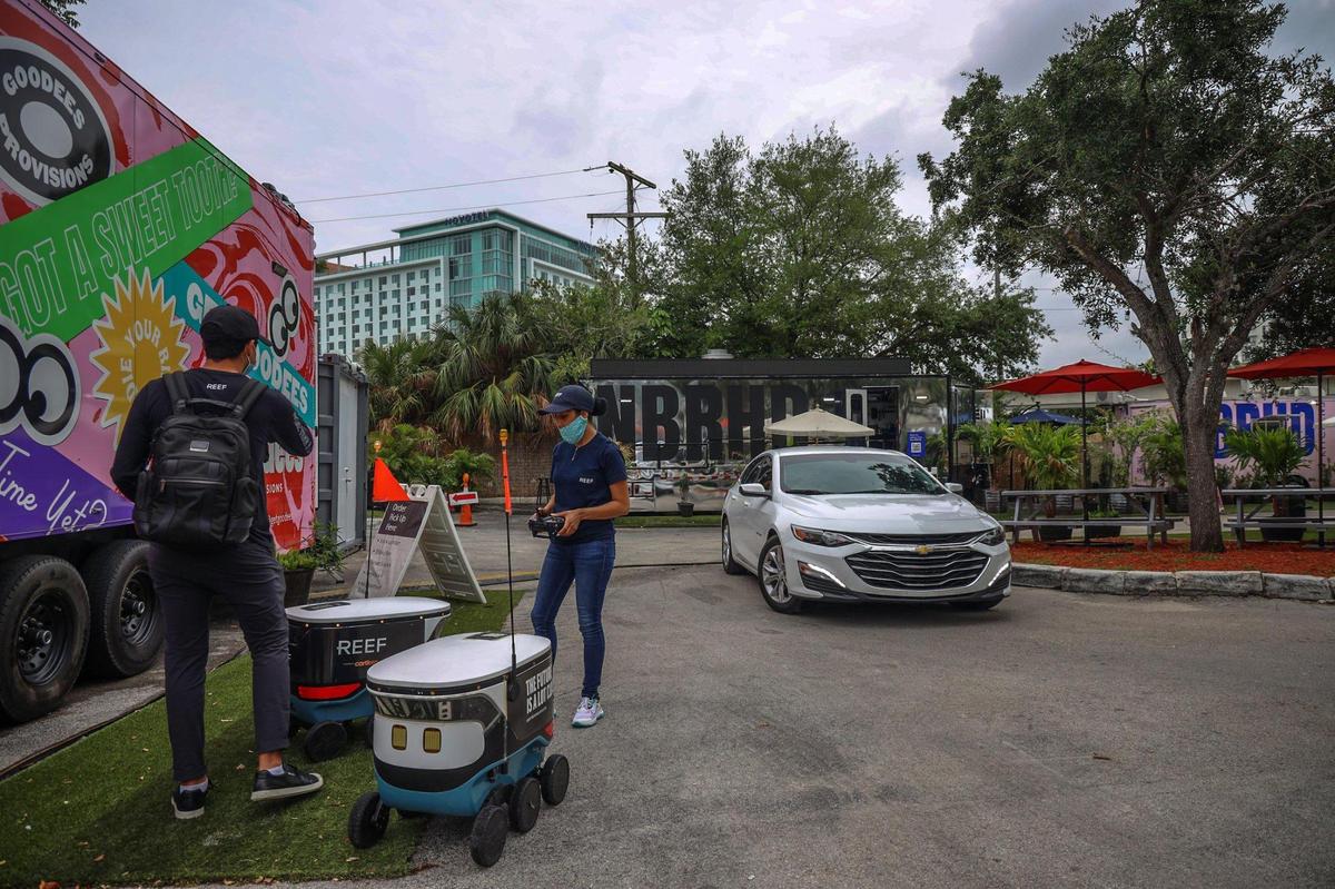Conductores de reparto y robots recogen comida de las cocinas móviles instaladas en un estacionamiento de Brickell el martes 20 de abril de 2021. Una empresa llamada REEF quiere poner en marcha más cocinas de este tipo en terrenos baldíos de toda la ciudad.