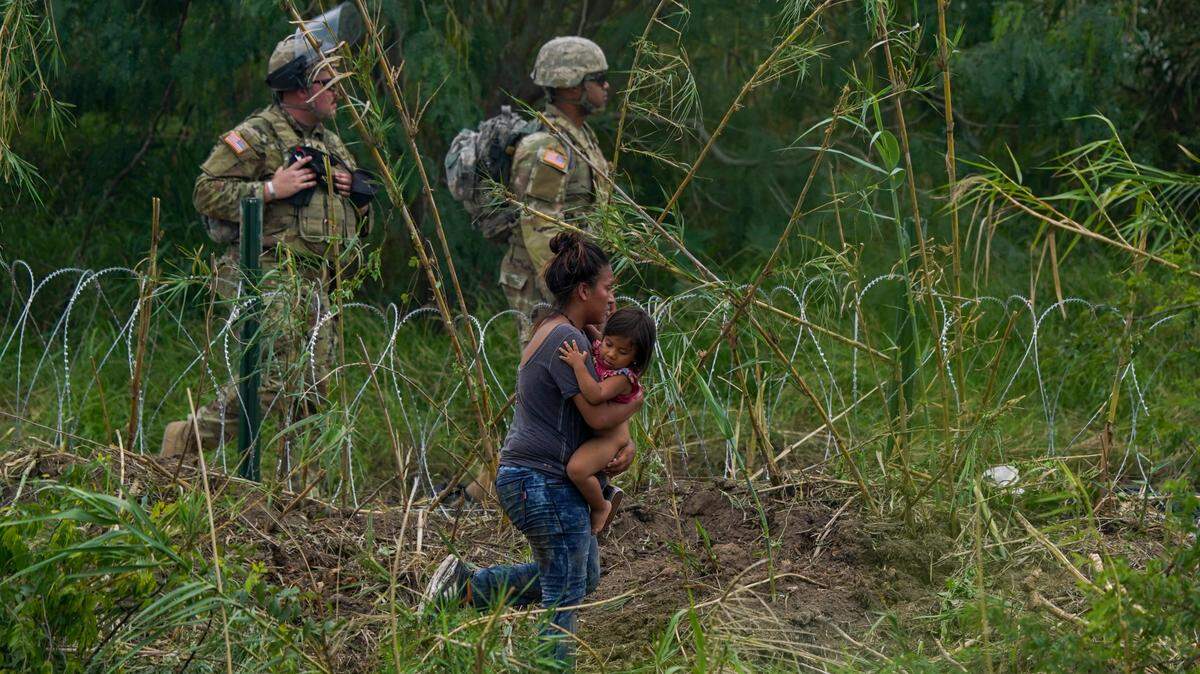Texas National Guardsmen stand along a stretch of razor wire as a migrant woman carrying a child tries to cross into the U.S, on the banks of the Rio Grande, as seen from Matamoros, Mexico, Thursday, May 11, 2023. Migrants rushed across the Mexico border Thursday in hopes of entering the U.S. in the final hours before pandemic-related asylum restrictions are lifted. (AP Photo/Fernando Llano)