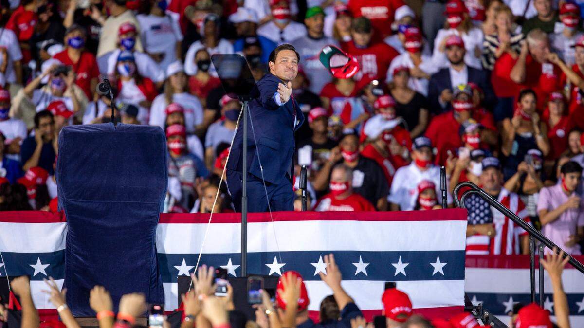 Gov. Ron DeSantis tosses MAGA hats into the crowd before taking the podium and imploring Floridians to vote for Donald Trump, during a Make America Great Again Victory Rally in November 2020.