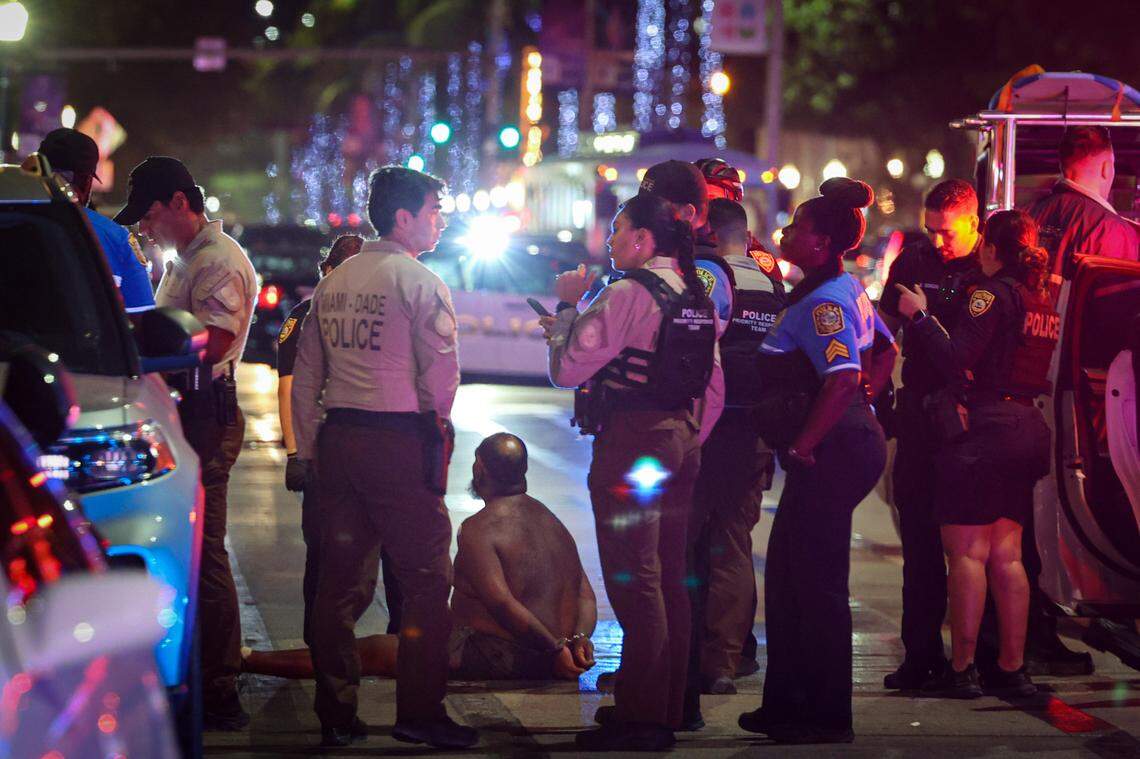 A man sits on a ground handcuffed Sunday night after witnesses say he had a knife. The detention came after a pair of deadly shootings over the weekend rocked this year’s spring break in Miami Beach.