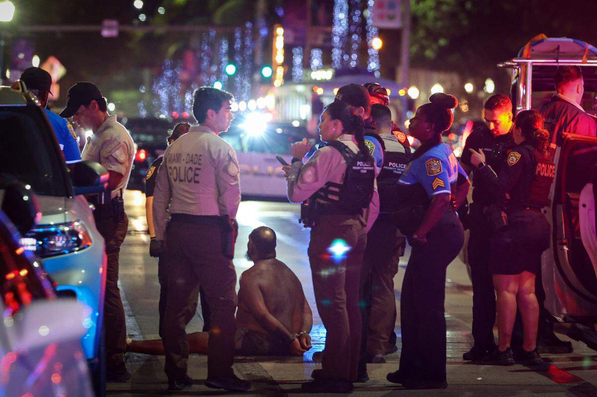 A man sits on the ground handcuffed after witnesses say he appeared to be brandishing a knife on Sunday, March 19, 2023, in Miami Beach.