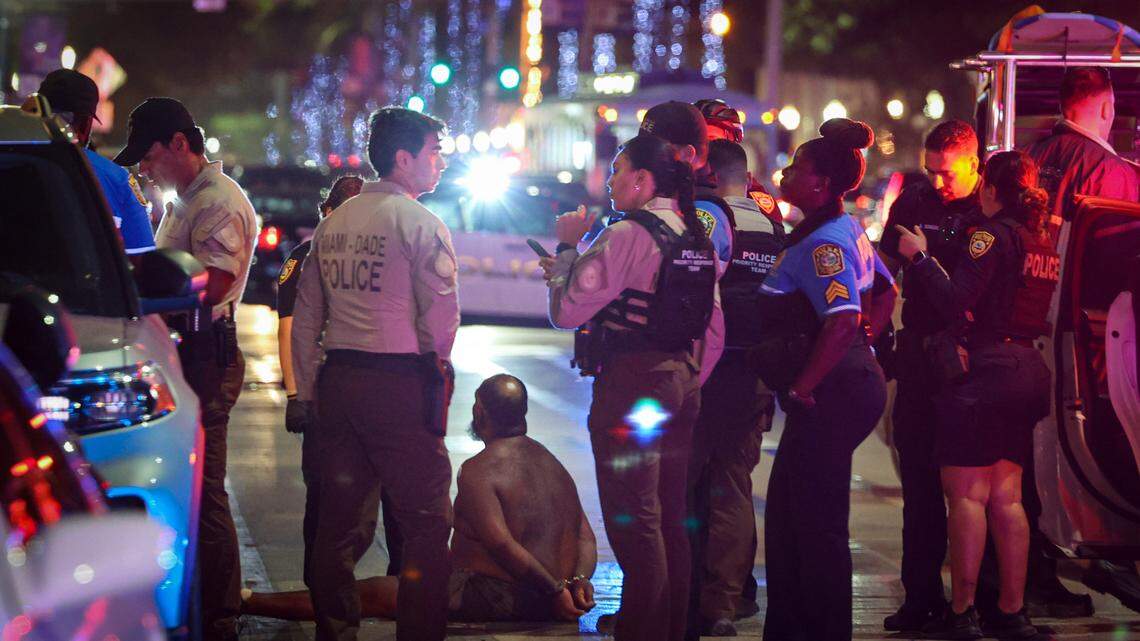 A man sits on a ground handcuffed Sunday night after witnesses say he had a knife. The detention came after a pair of deadly shootings over the weekend rocked this year’s Spring Break on Miami Beach.